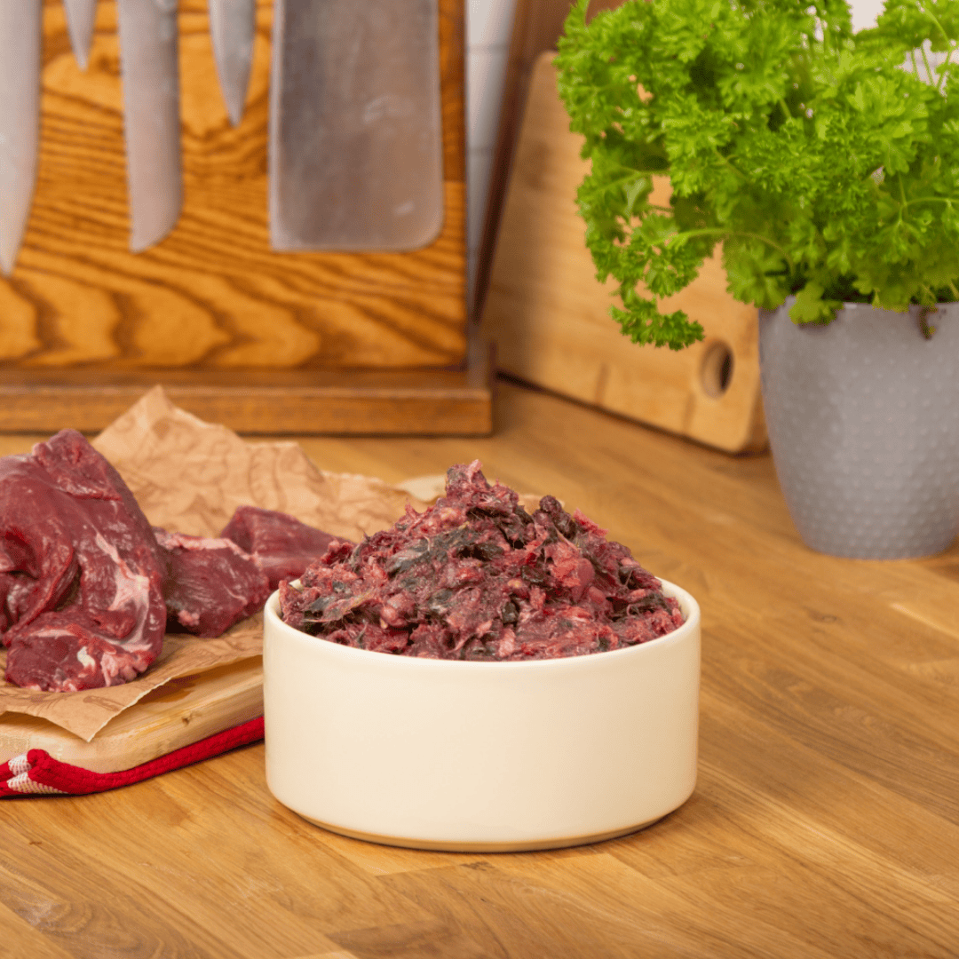 The Dogs Butcher Venison mince boneless raw dog food in a bowl placed next to raw venison 